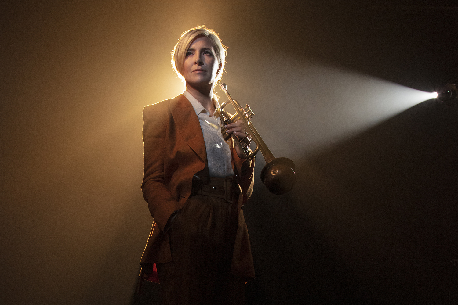 A woman wearing a suit and holding a trumpet with a spotlight on her