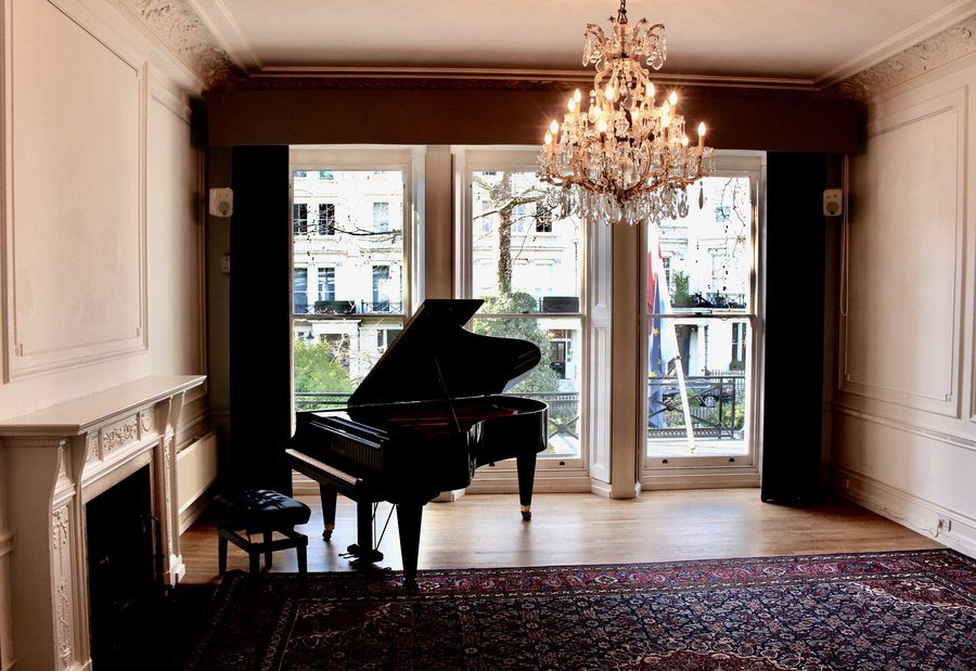 A grand piano in a room with a large rug and a chandelier and fireplace