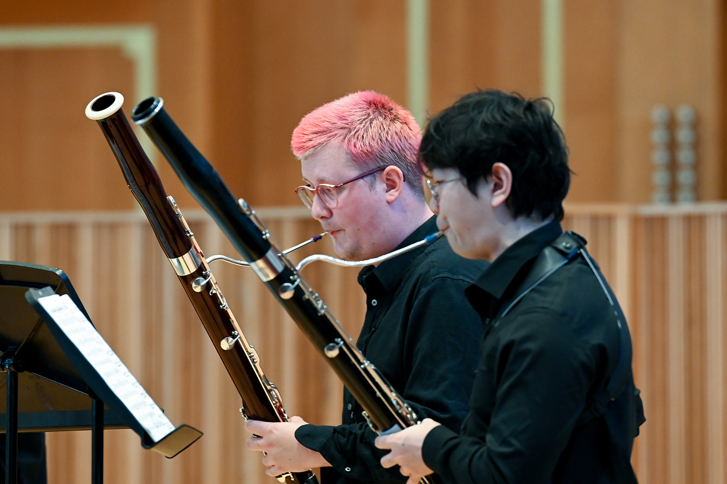 Two students, one with pink hair one with black hair, performing on bassoons in the Amaryllis Fleming Concert Hall