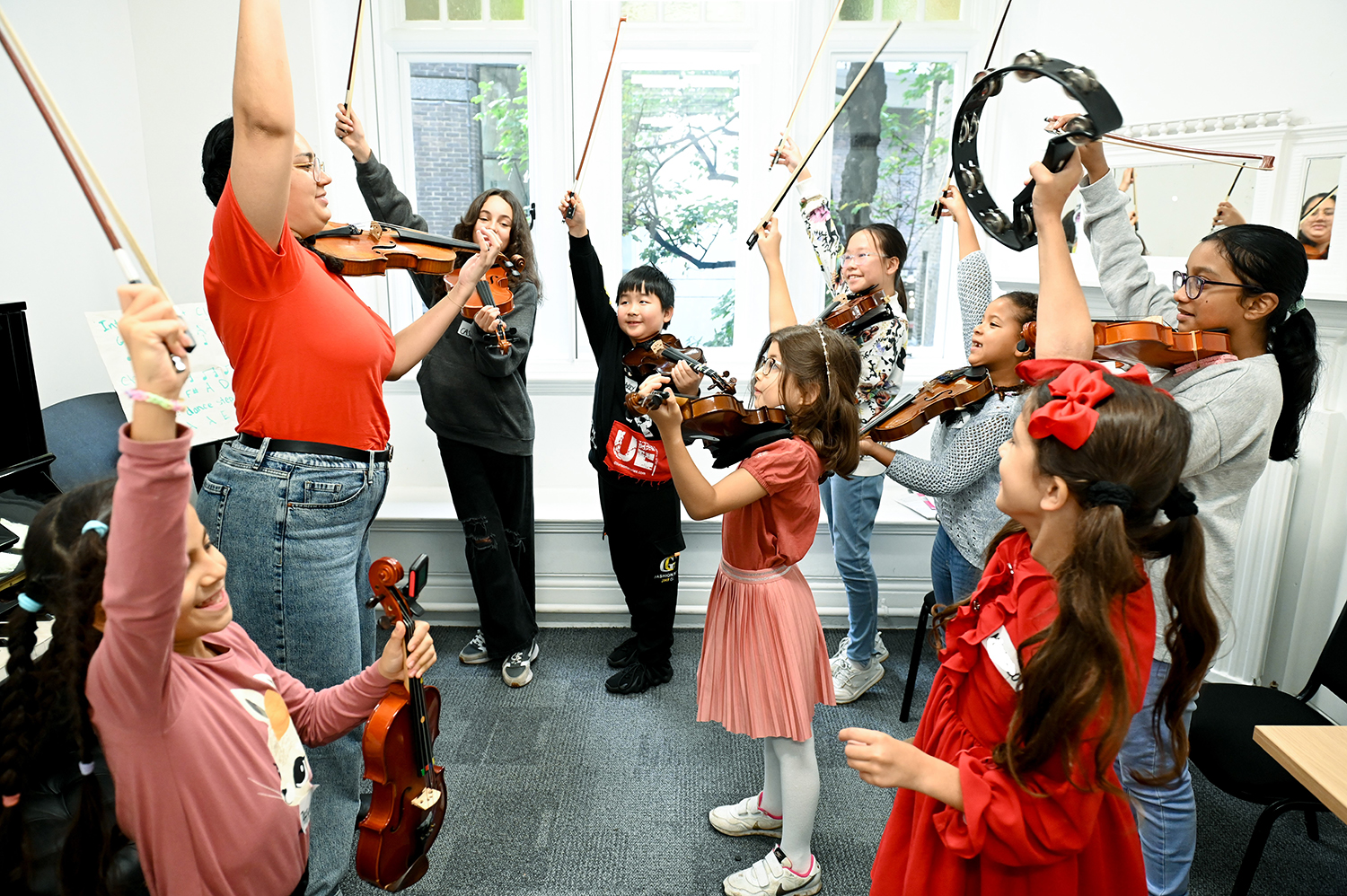 Children holding bows of a violin and tambourines in the air with an H漫画 Sparks member