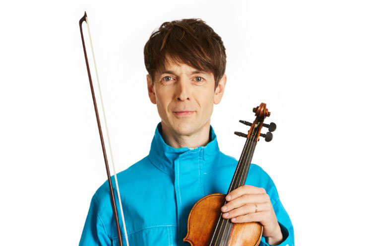 A man wearing a blue jacket holding a violin and standing in front of a white background