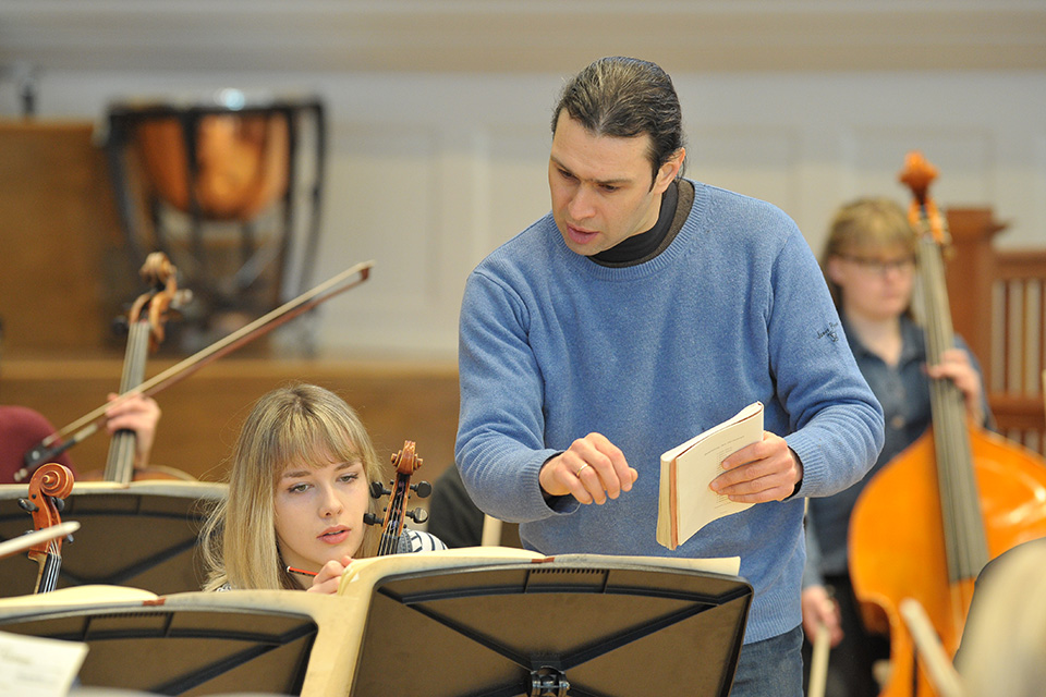 Vladimir Jurowski, a man with dark hair, pointing at a student's music with two students looking at the music, holding their instruments.